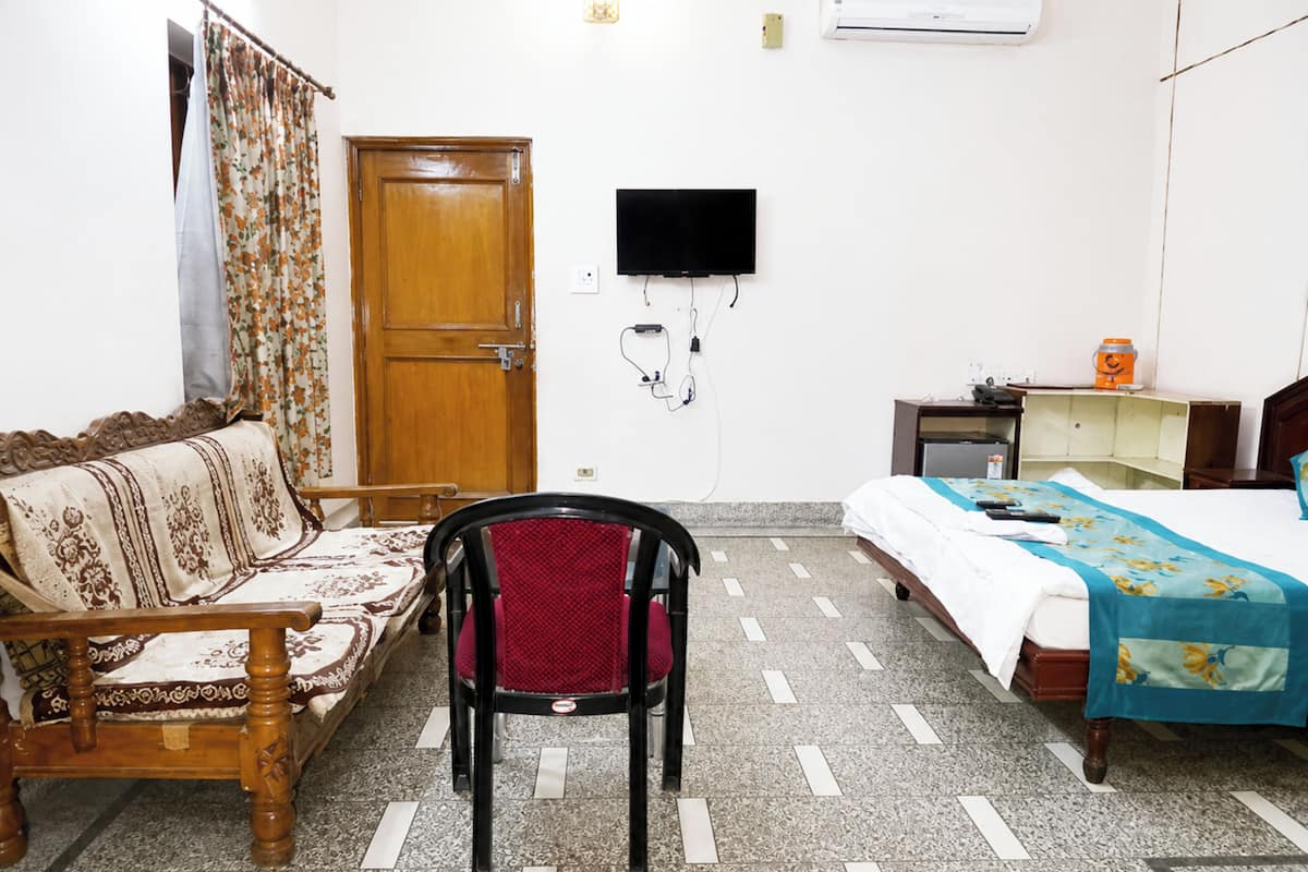 Quarto com cama de madeira, um sofá de madeira, uma cadeira vermelha, televisão na parede e chão em mosaico.