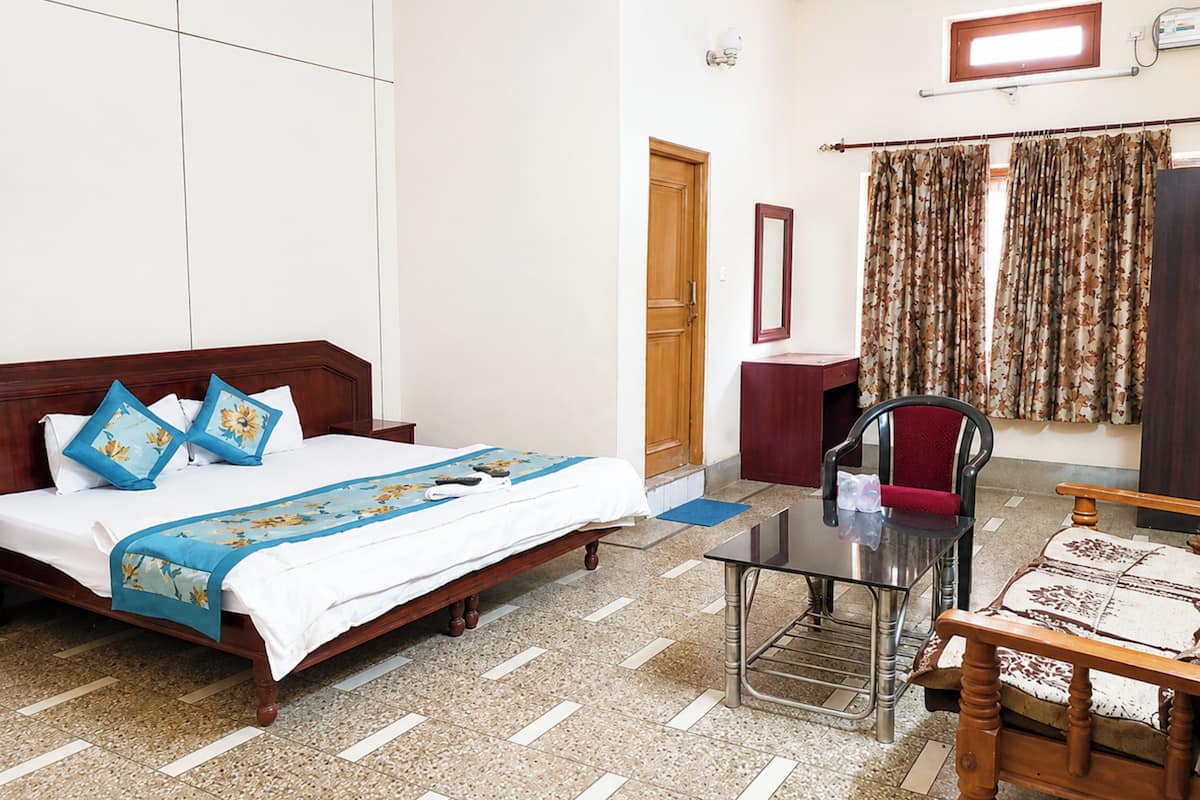 Quarto de hotel com cama, escrivaninha, cadeira, espelho e janela com cortinas.