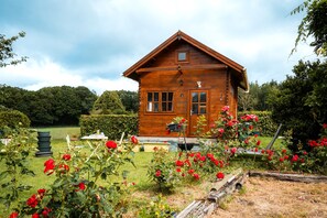 A wooden cabin with a pitched roof, surrounded by a garden with red roses.