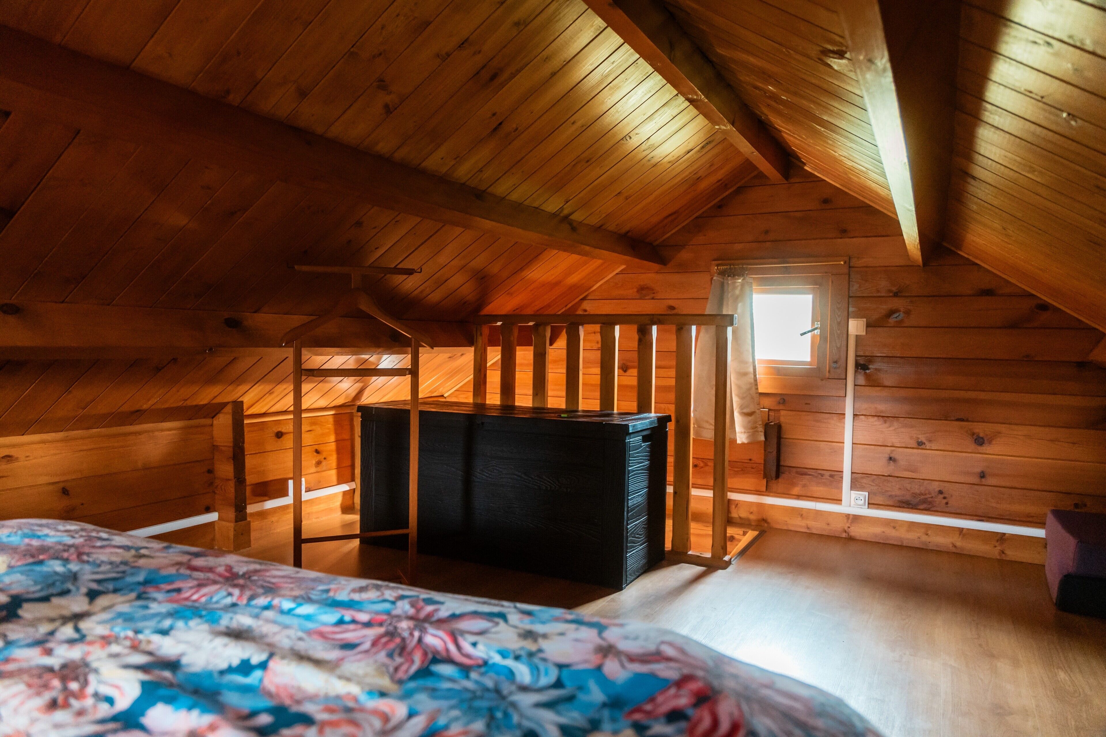 A wooden cabin room with a bed, a dresser, and a window.