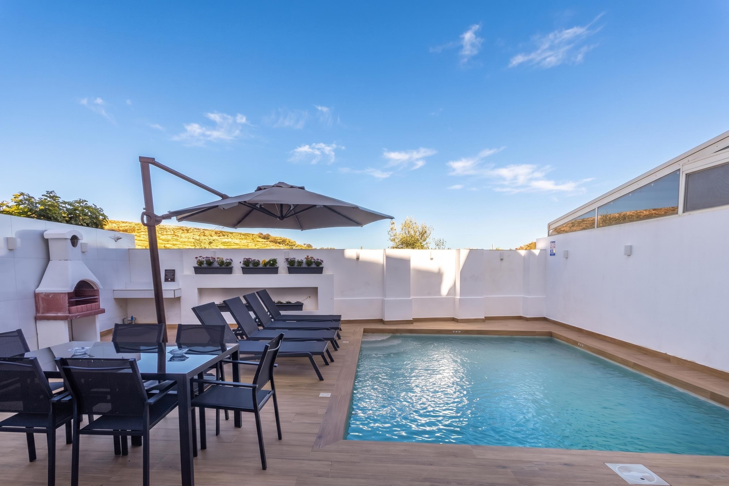 A poolside area with lounge chairs, a table, and a barbecue grill.
