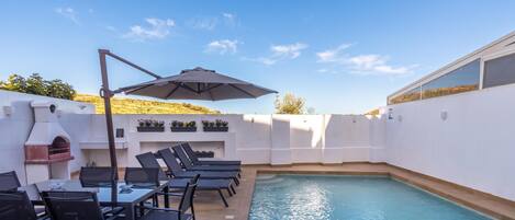 A poolside area with lounge chairs, a table, and a barbecue grill.