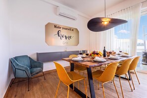 A modern dining room with a wooden table set for four, yellow chairs, a blue sofa, and a decorative wall sign. - Dar Sara Holiday Gozitan Home (Victoria)
