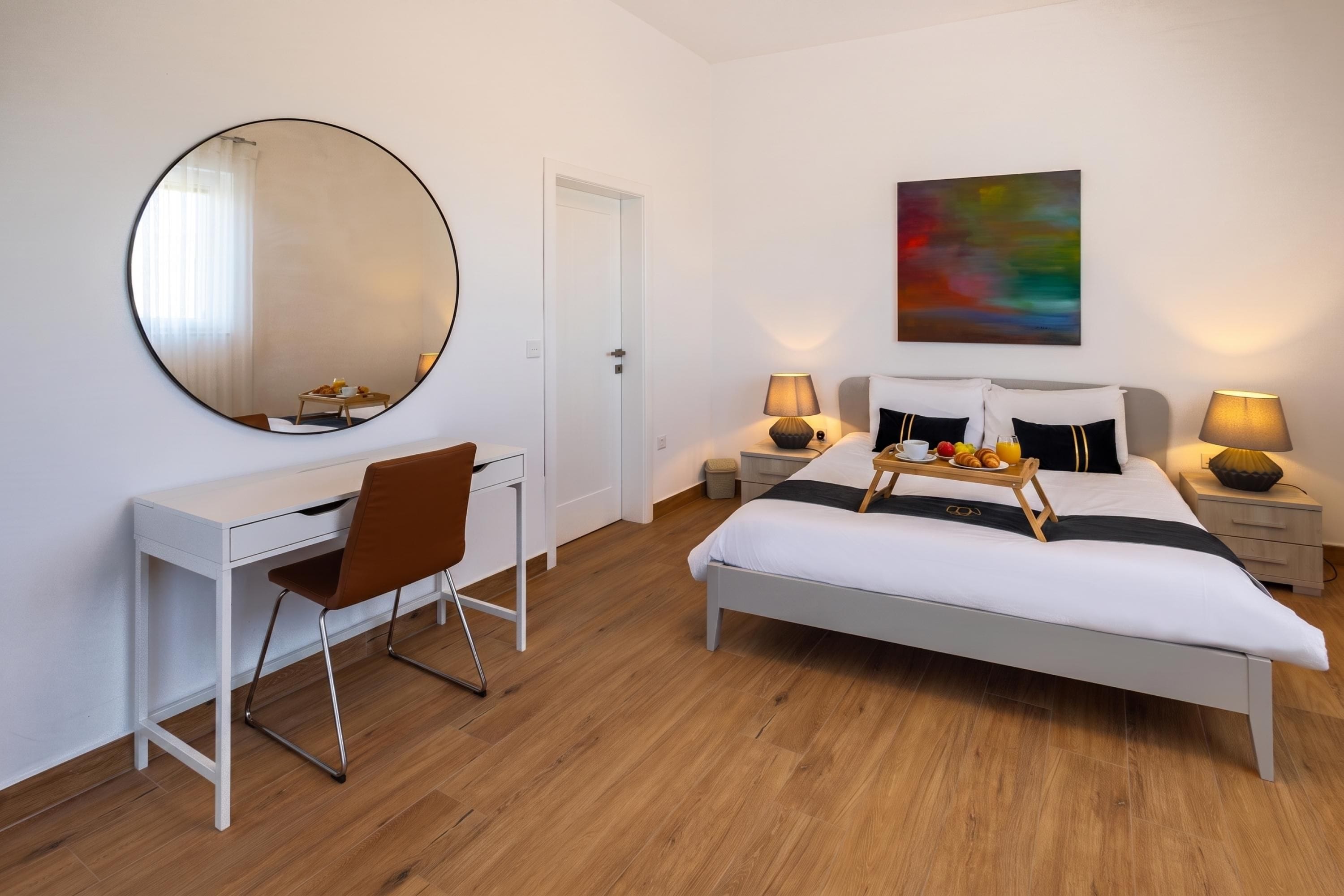 A modern bedroom with a bed, bedside tables, a desk, a chair, and a large mirror.