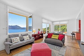 A modern living room with a sofa, ottoman, and a dining area with a kitchen counter. - Villa Alessia - 4 bed Villa With Lake Maggiore View (Stresa)