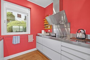 A kitchen with red walls, a stainless steel range hood, and a window with a view of greenery. - Villa Alessia - 4 bed Villa With Lake Maggiore View (Stresa)