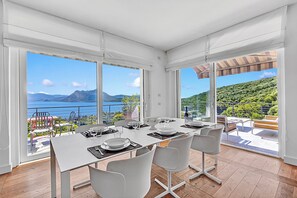 Spiseområde med et bord dækket til fire personer, store vinduer og udsigt til havet og bjergene.