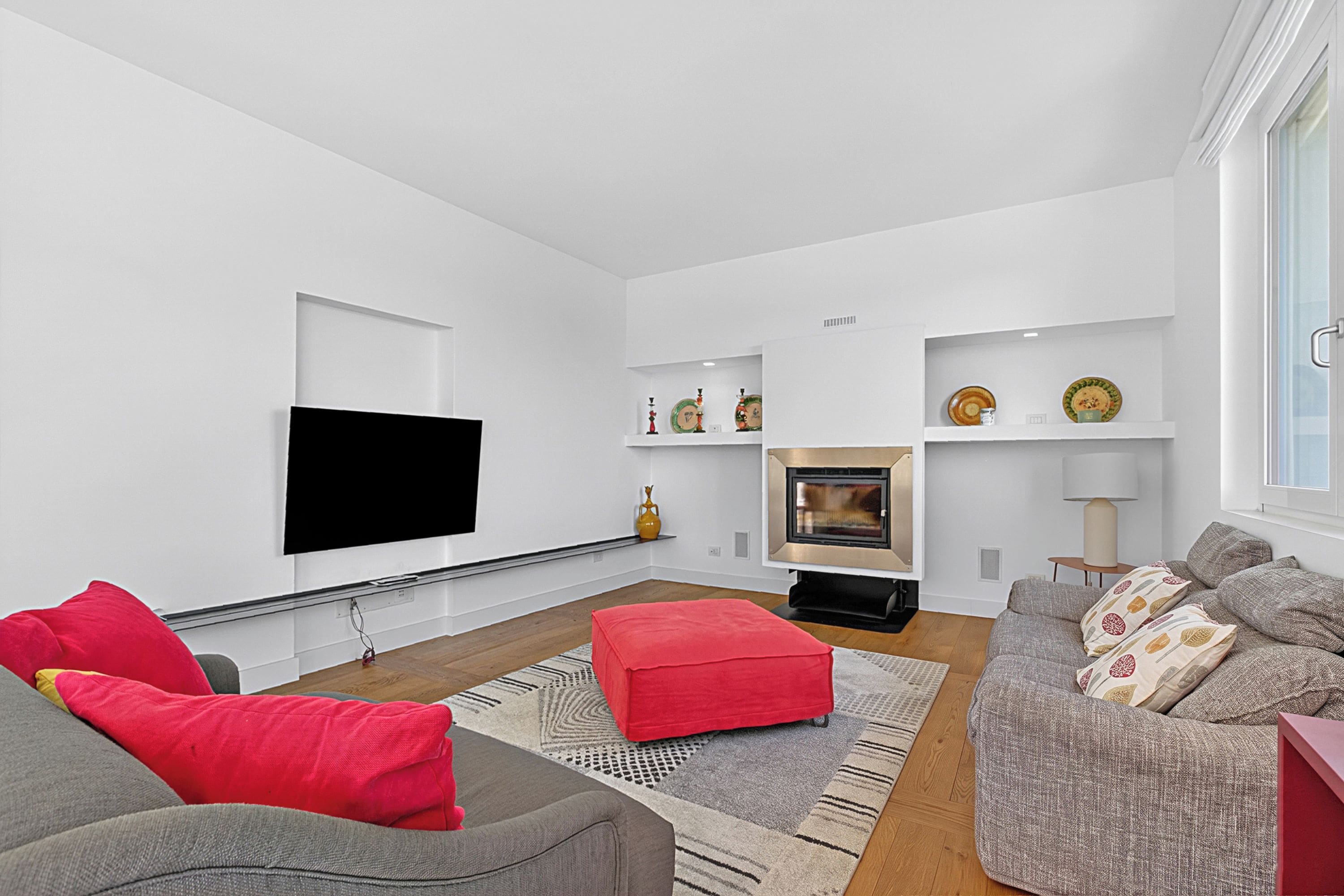 Una sala de estar moderna con un televisor de pantalla plana, una chimenea y un sofá con cojines rojos.