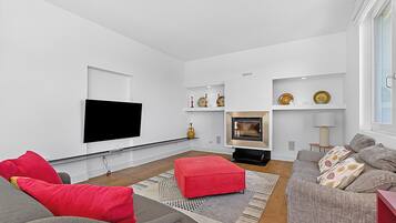Una sala de estar moderna con un televisor de pantalla plana, una chimenea y un sofá con cojines rojos.