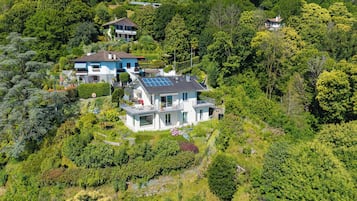 A hillside property with multiple houses, lush greenery, and a prominent house with a solar panel roof.
