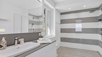 A modern bathroom with a large mirror, a white sink, a shower, and a view of the outdoors.