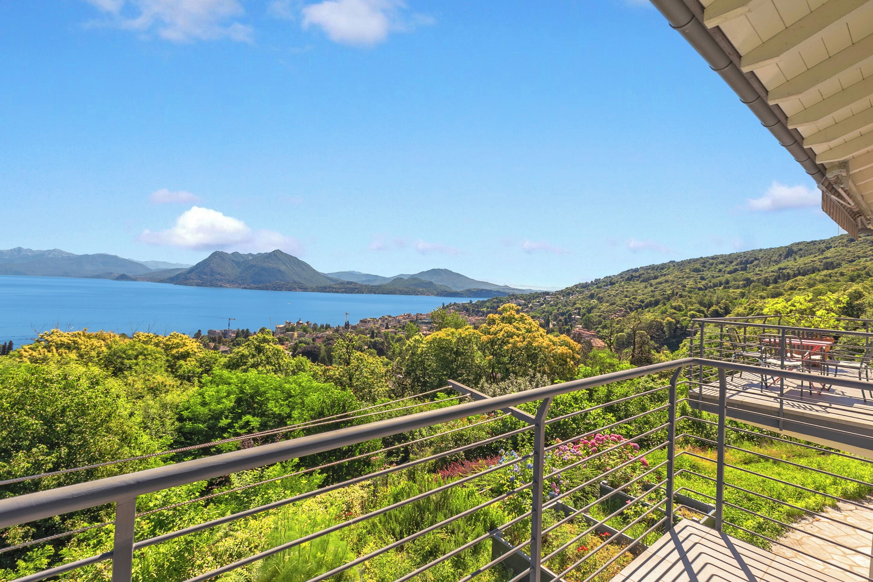 A balcony with a view of a lake, mountains, and greenery.