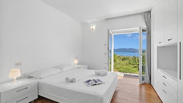 A bedroom with a bed, bedside tables, a lamp, a magazine, and a view of the sea.