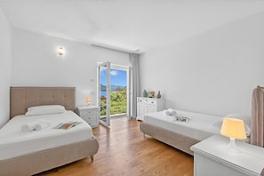Habitación de hotel con dos camas, una mesita de noche, una lámpara y vistas al exterior.