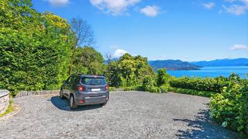 A car parked on a cobblestone driveway with a scenic view of mountains and a lake.