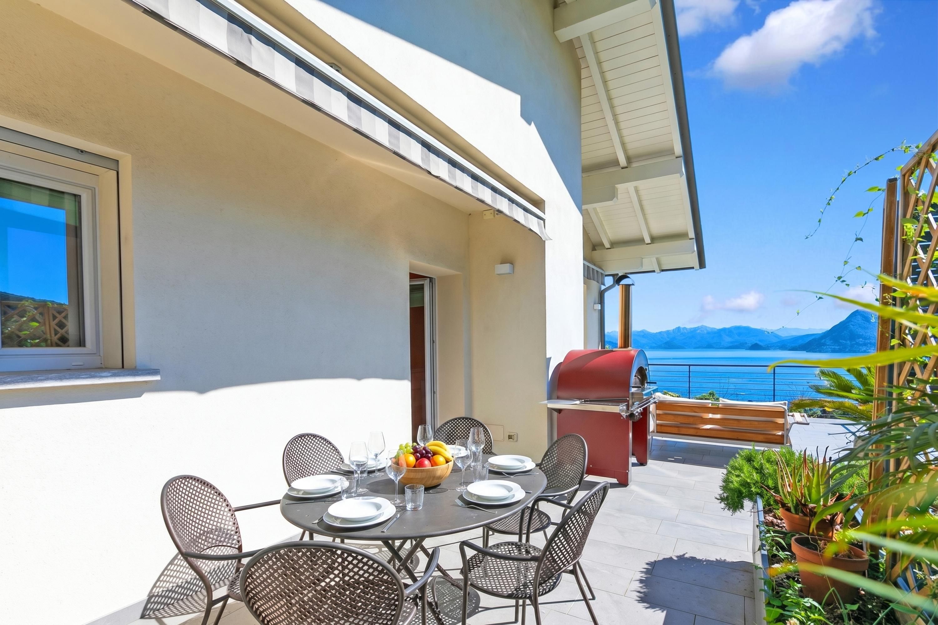 Comedor con mesa dispuesta para seis personas, asientos exteriores, una parrilla y vista al mar.