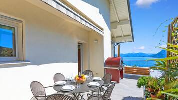 Comedor con mesa dispuesta para seis personas, asientos exteriores, una parrilla y vista al mar.