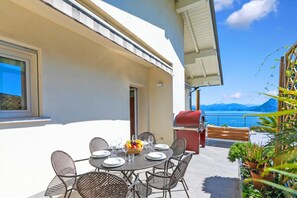 A dining area with a table set for six, outdoor seating, a grill, and a view of the sea. - Villa Alessia - 4 bed Villa With Lake Maggiore View (Stresa)