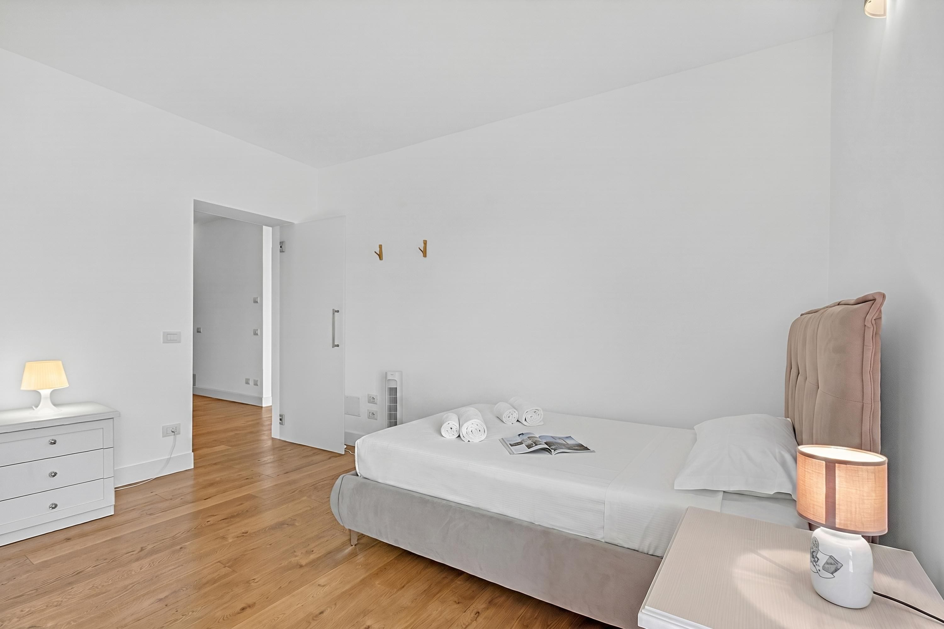 A modern bedroom with a bed, bedside table, lamp, and a dresser.