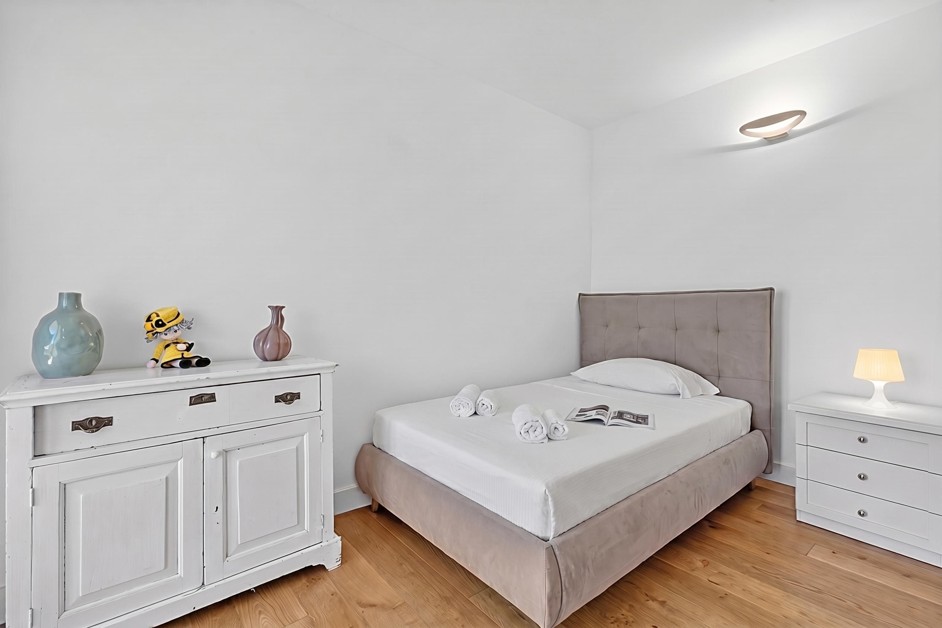 Un dormitorio con cama, mesitas de noche, cómoda y objetos decorativos.