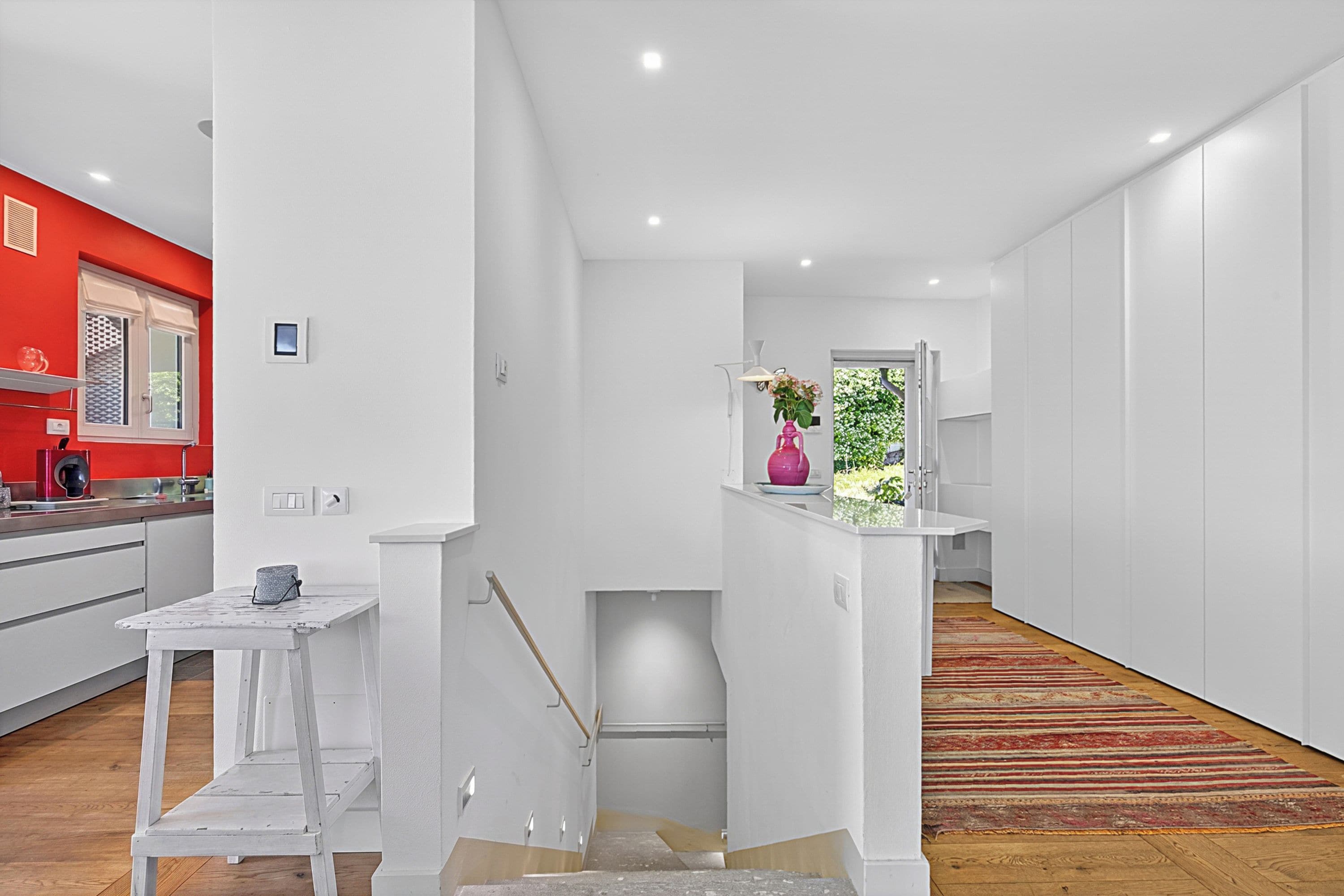A modern interior with a kitchen, a staircase, and a hallway leading to a room with a view.
