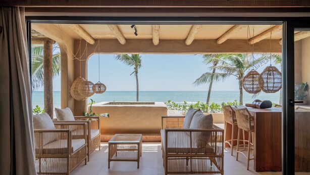 A room with wicker furniture, a wooden table, and a view of the ocean.