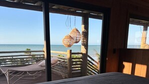 A bedroom with a bed, a view of the ocean, and a balcony with wicker furniture.