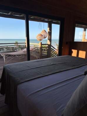 A bedroom with a bed, a view of the ocean, and a balcony with wicker furniture.