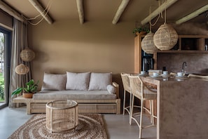 A modern living area with a sofa, wicker chairs, a coffee table, and a kitchen area with a bar.