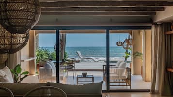 A room with a view of the sea, furnished with wicker chairs and a sofa, and a large woven light fixture.