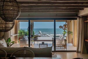 Una habitación con vista al mar, amueblada con sillas de mimbre y un sofá, y una lámpara de techo grande hecha con fibras naturales.