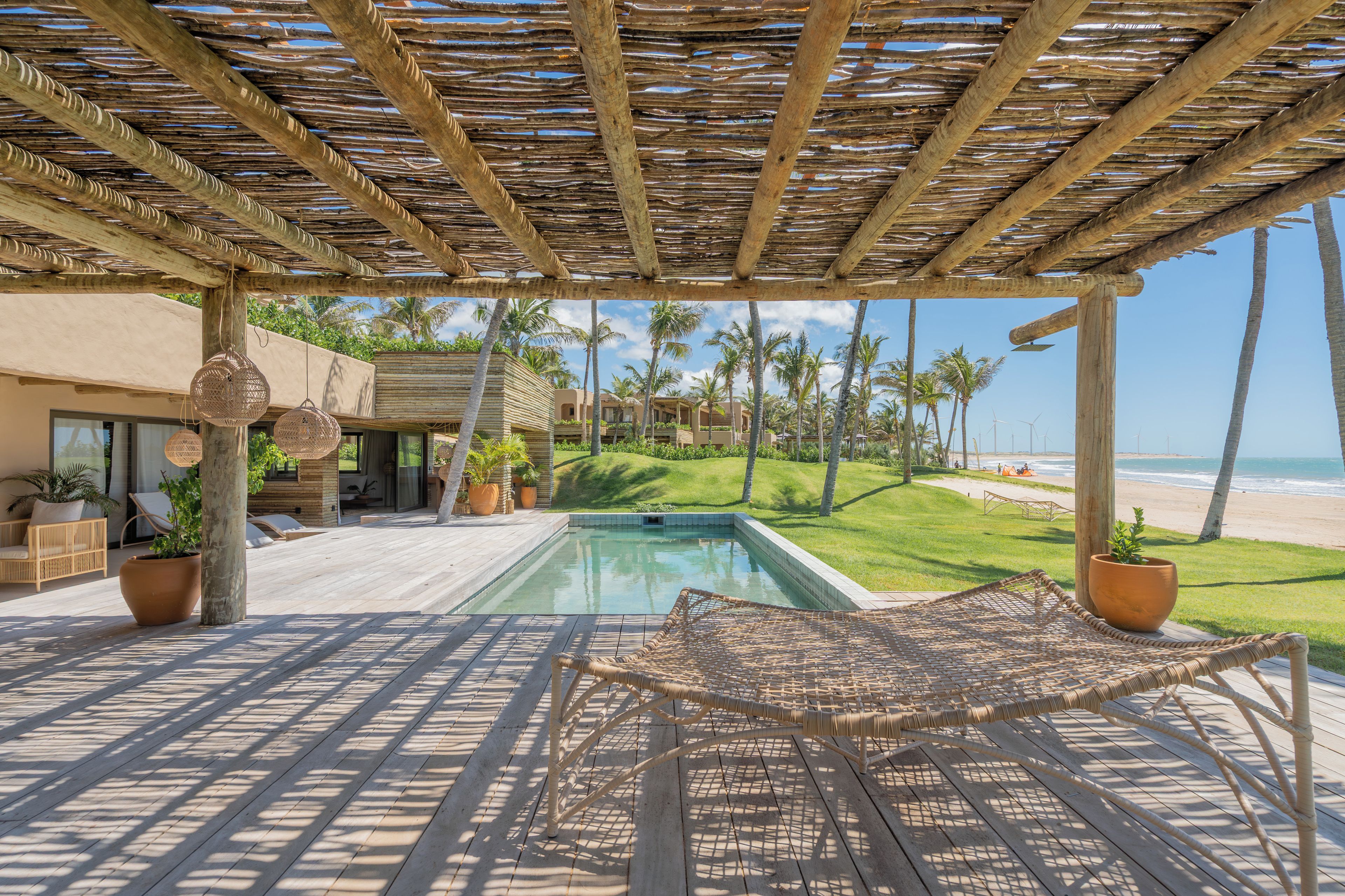 Zona junto a la piscina con una pérgola, sillones de descanso y vistas a la playa.