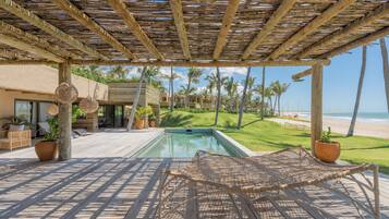 Zona junto a la piscina con una pérgola, sillones de descanso y vistas a la playa.