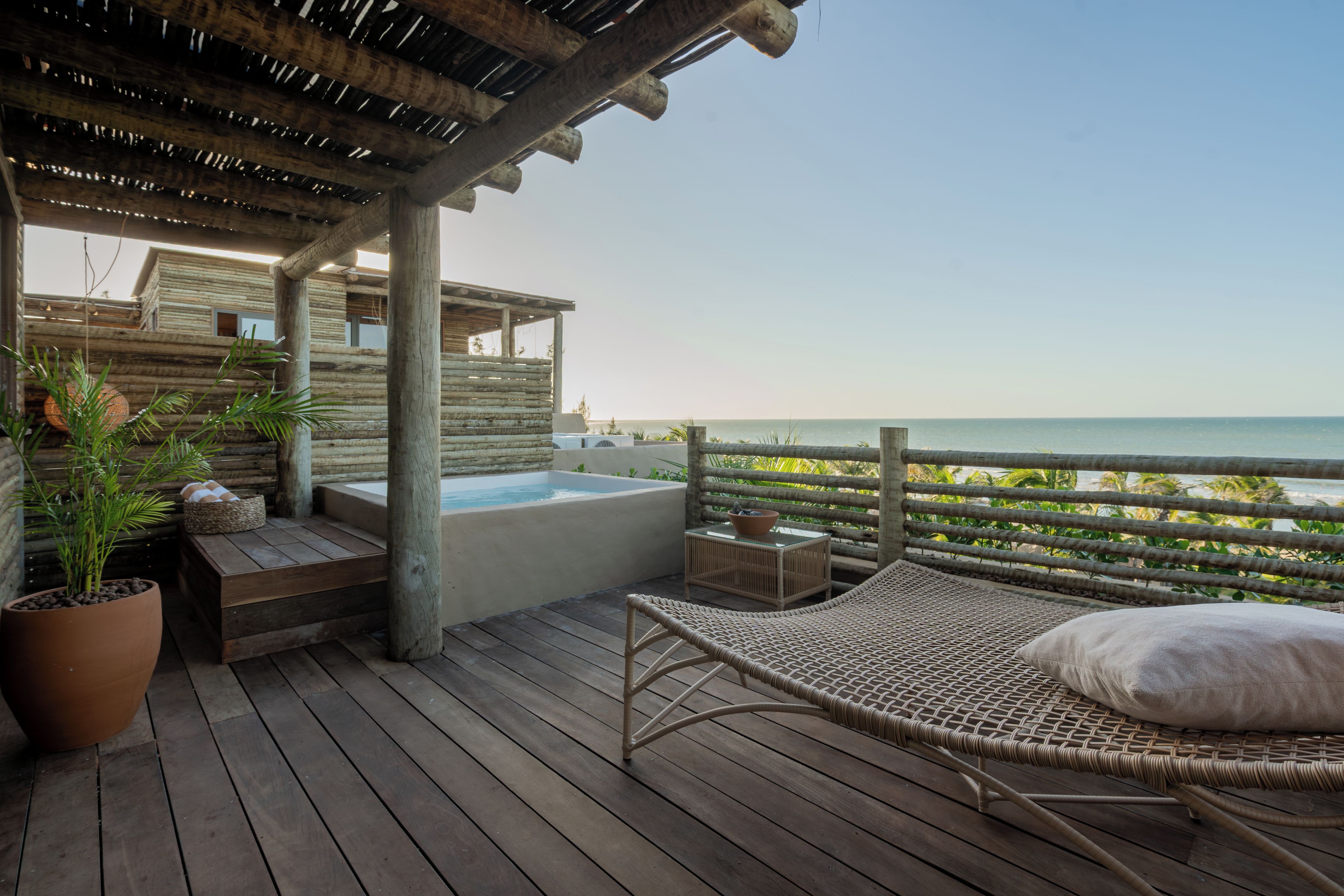 Una terraza de madera con un jacuzzi, sillas de descanso y vista al océano.