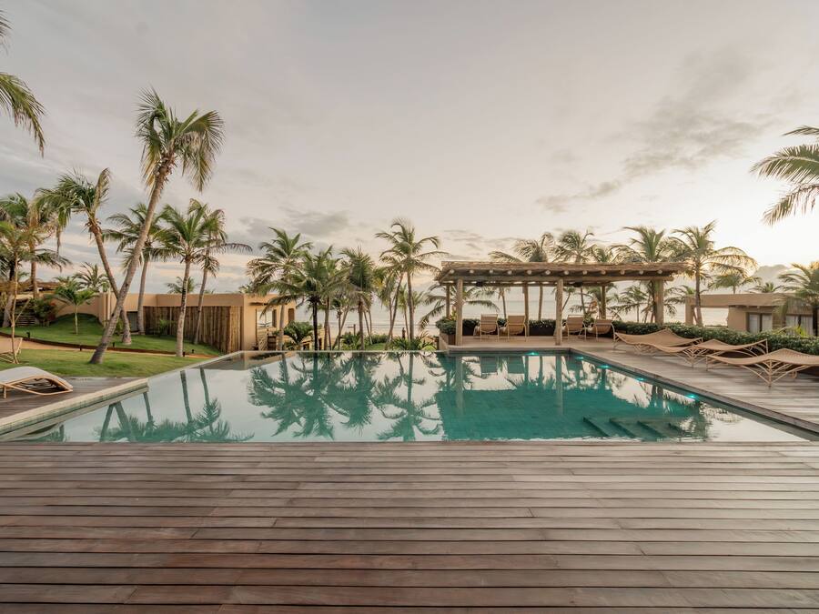 Ein Poolbereich mit Holzterrasse, Liegestühlen und Palmen.