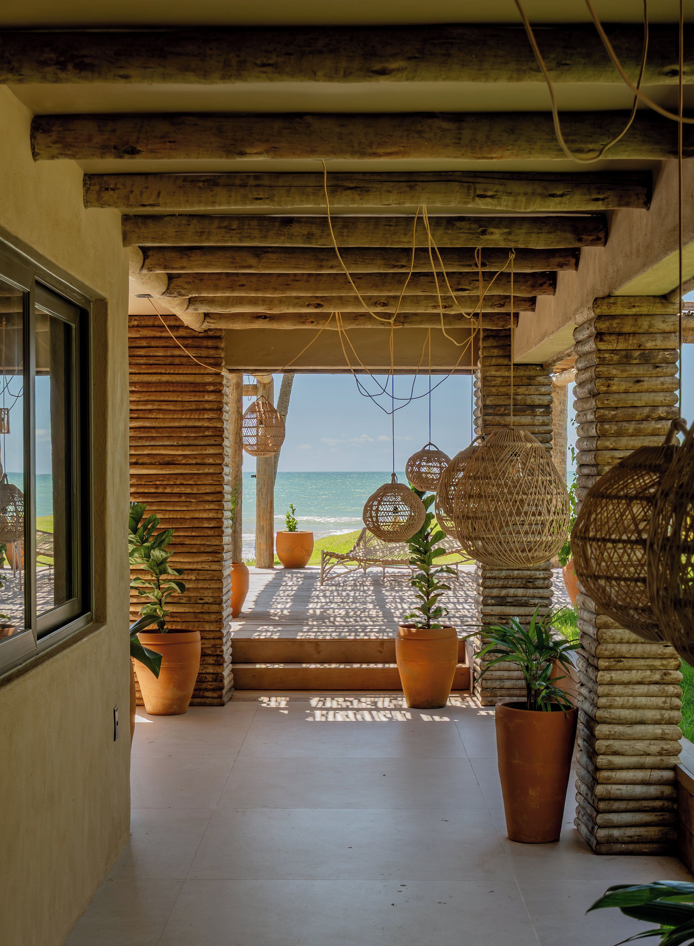 A covered outdoor area with wooden beams, potted plants, and wicker furniture.