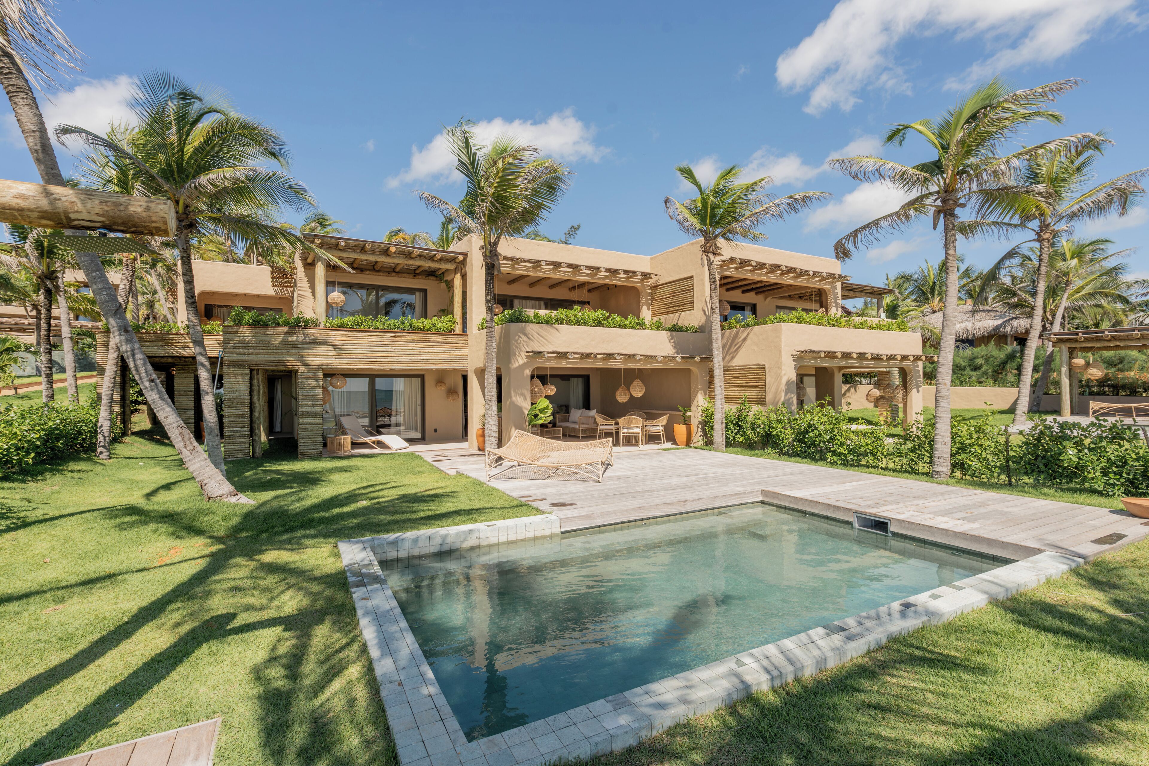 A resort with a swimming pool, palm trees, and a covered outdoor seating area.
