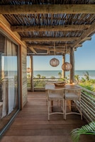 Una terraza de madera con mesa y sillas, con vista a la playa.