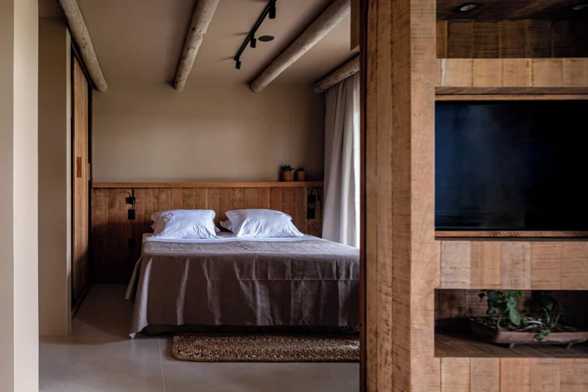 A bedroom with a bed, wooden headboard, and a small shelf with plants.