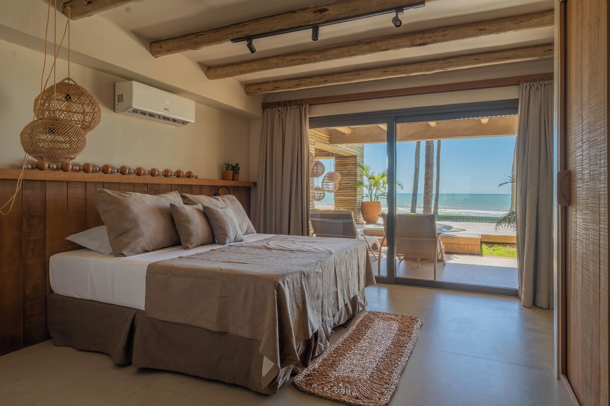Un dormitorio con cama, ventana con cortinas, ventilador de techo y vista al océano.