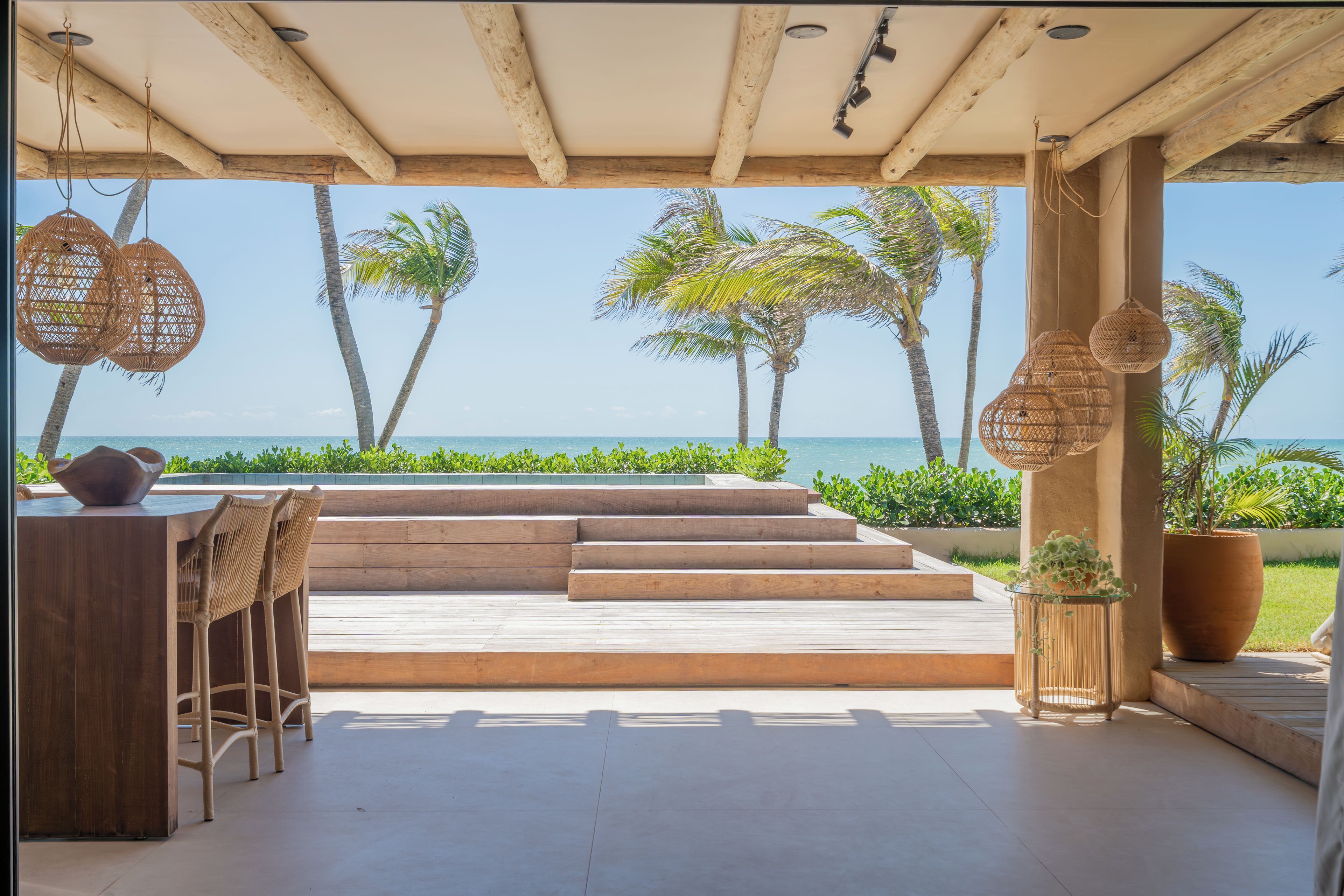 An outdoor seating area with a view of the ocean, wooden steps, and hanging wicker lamps.