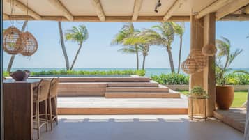 An outdoor seating area with a view of the ocean, wooden steps, and hanging wicker lamps.