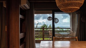 A room with a wooden table, wicker chairs, and a view of the ocean through a large window.