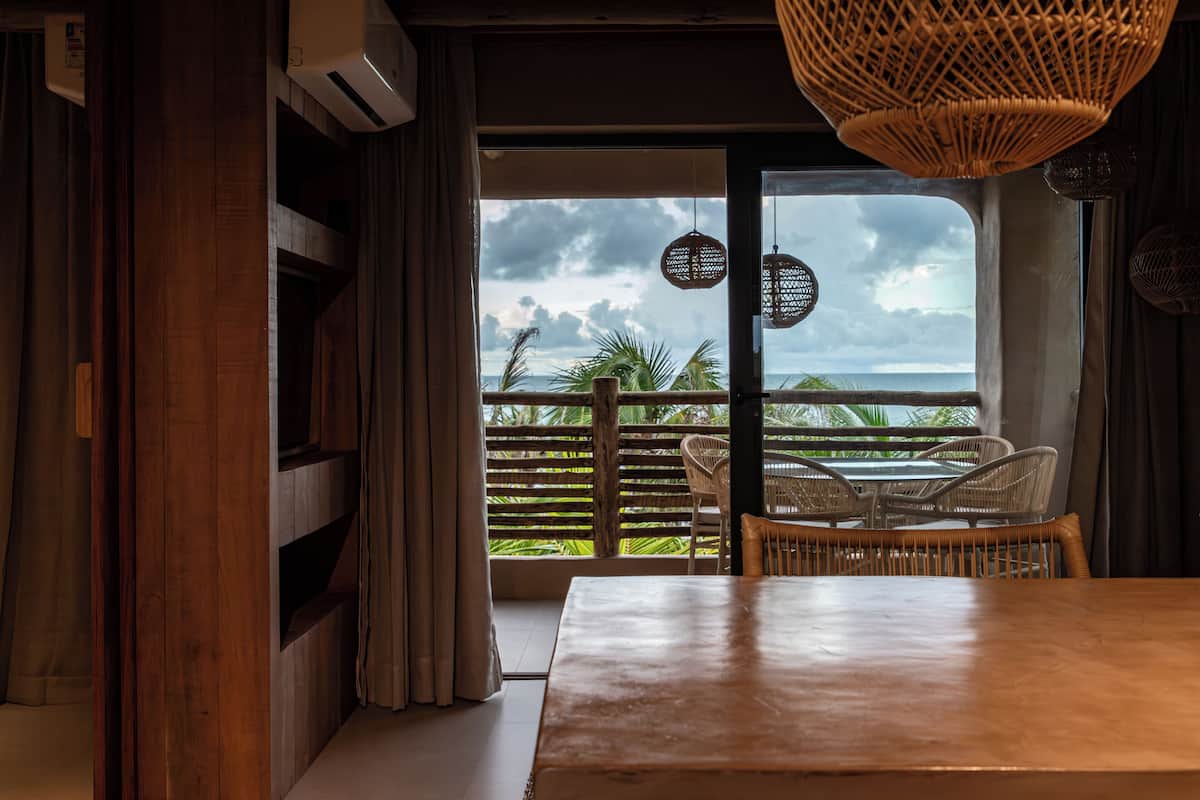 A room with a wooden table, wicker chairs, and a view of the ocean through a large window.