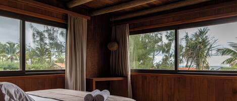 A room with a bed, wooden walls, large windows, and a view of palm trees.