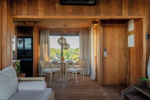 Un interior de madera con comedor, sofá y vistas por una ventana.