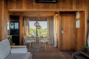 Interior em madeira com área de refeições, um sofá e vista pela janela.