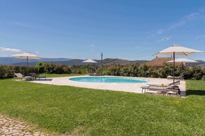 A swimming pool with lounge chairs and umbrellas, surrounded by a well-maintained lawn and hills in the background.