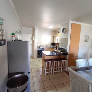 Une cuisine compacte équipée d’un réfrigérateur, d’une cuisinière et d’un évier. On y trouve des tabourets au comptoir et une table à manger avec des chaises.