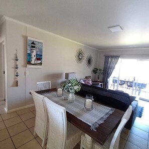 Un comedor con mesa de madera, sillas blancas y un cuadro de un faro.